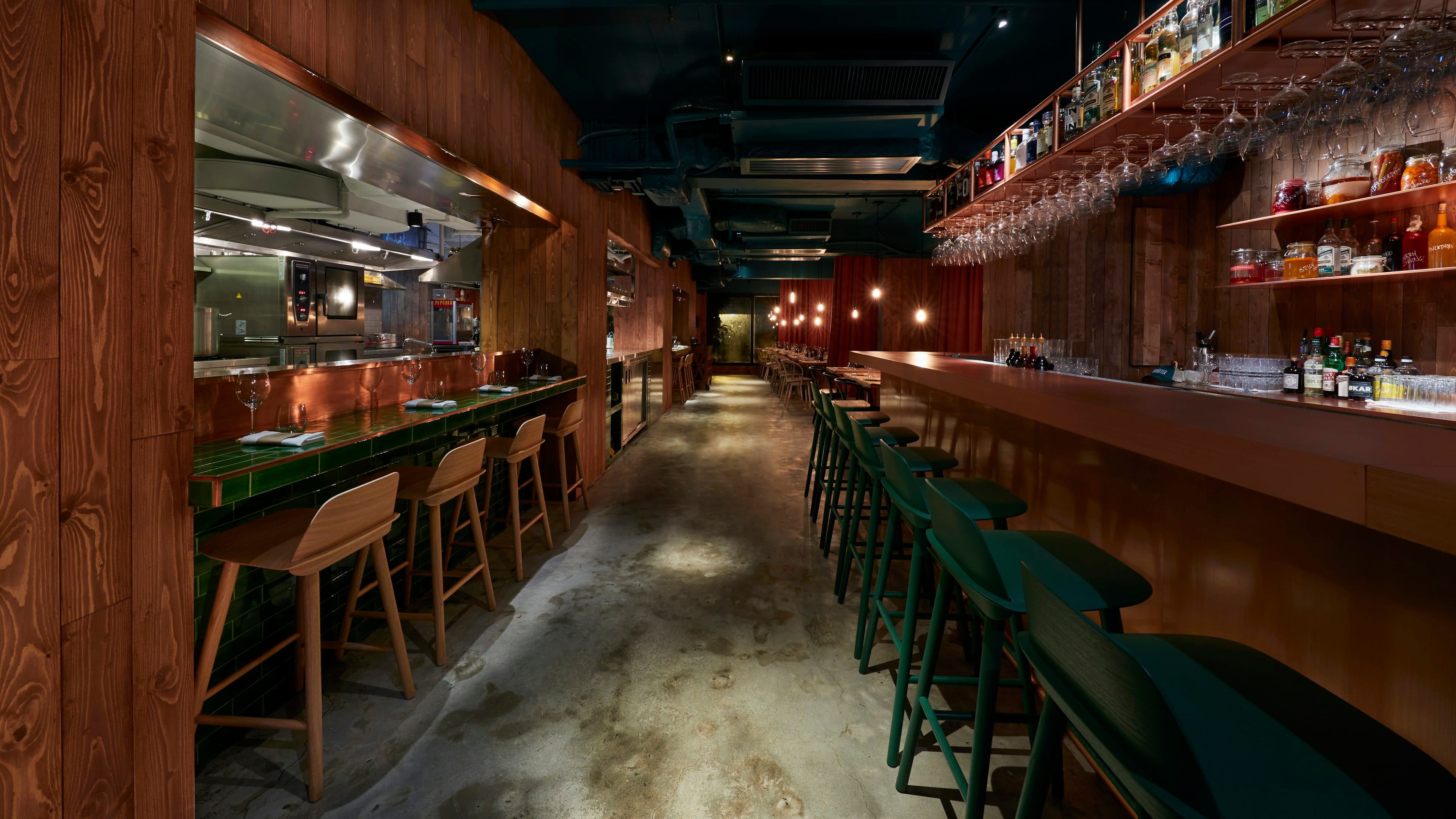 The oak counter at Heron & Salt at dusk, with the kitchen lit behind it